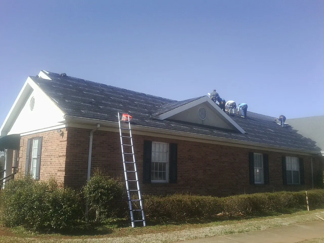 Crew tearing shingles off a brick ranch roof with a ladder set — Emergency Roof Repair work by our crew in Cedar Glen