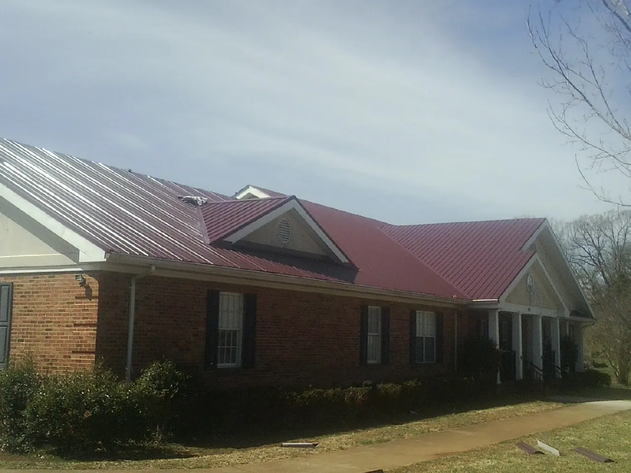Red metal roof with gabled entries on a long brick building, from a Hail Damage Roof Repair job in Cedar Glen