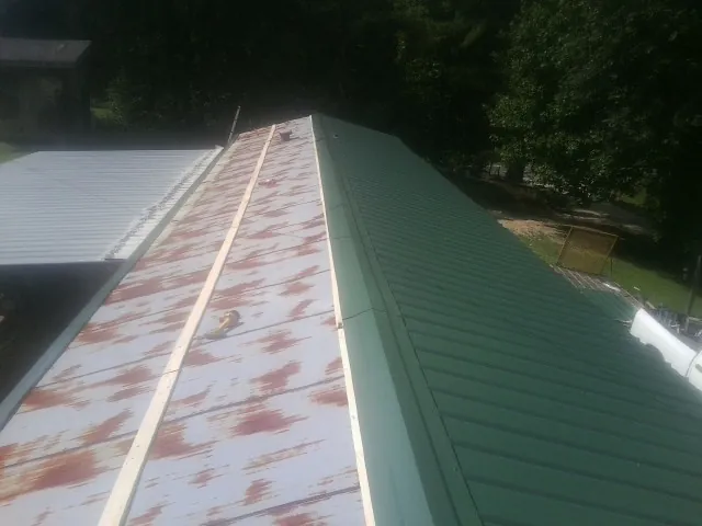 Old rusted panels beside newly installed green metal roofing — Wind Damage Roof Repair by Roofing Brothers in Cedar Glen