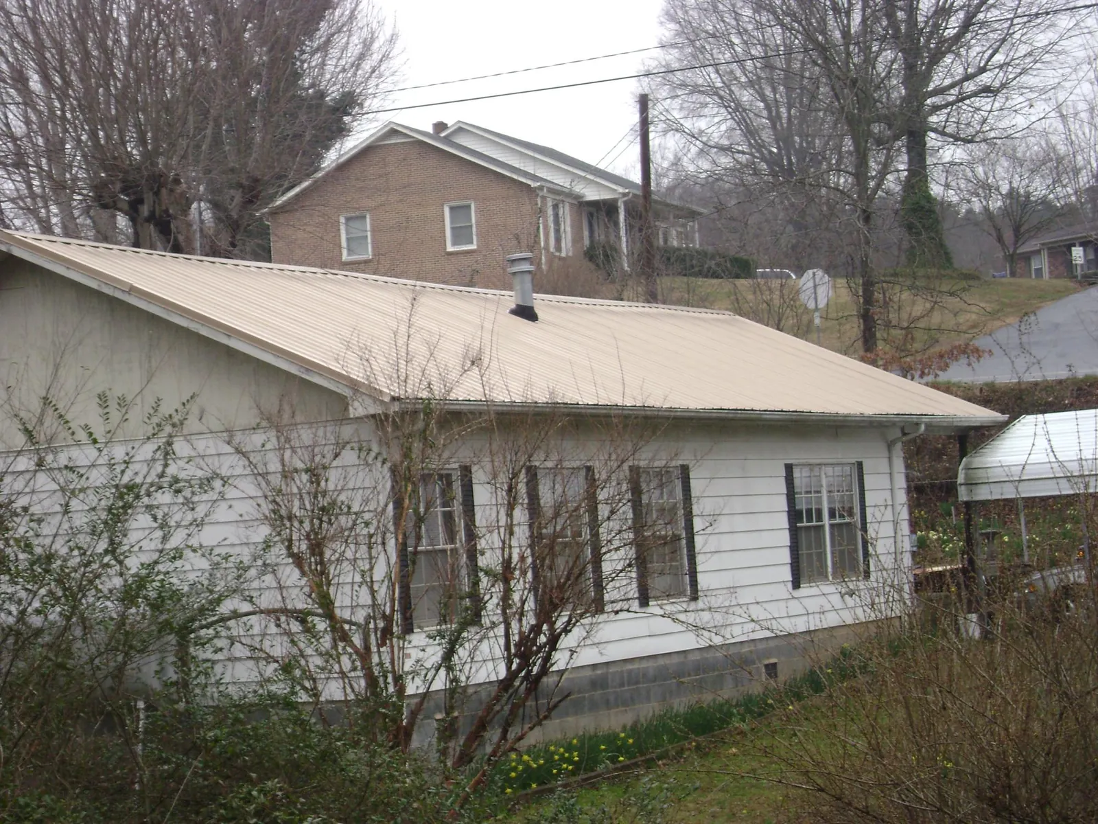 Tan metal roof on a white sided house set into a hillside — Commercial Roofing by Roofing Brothers in Cedar Glen