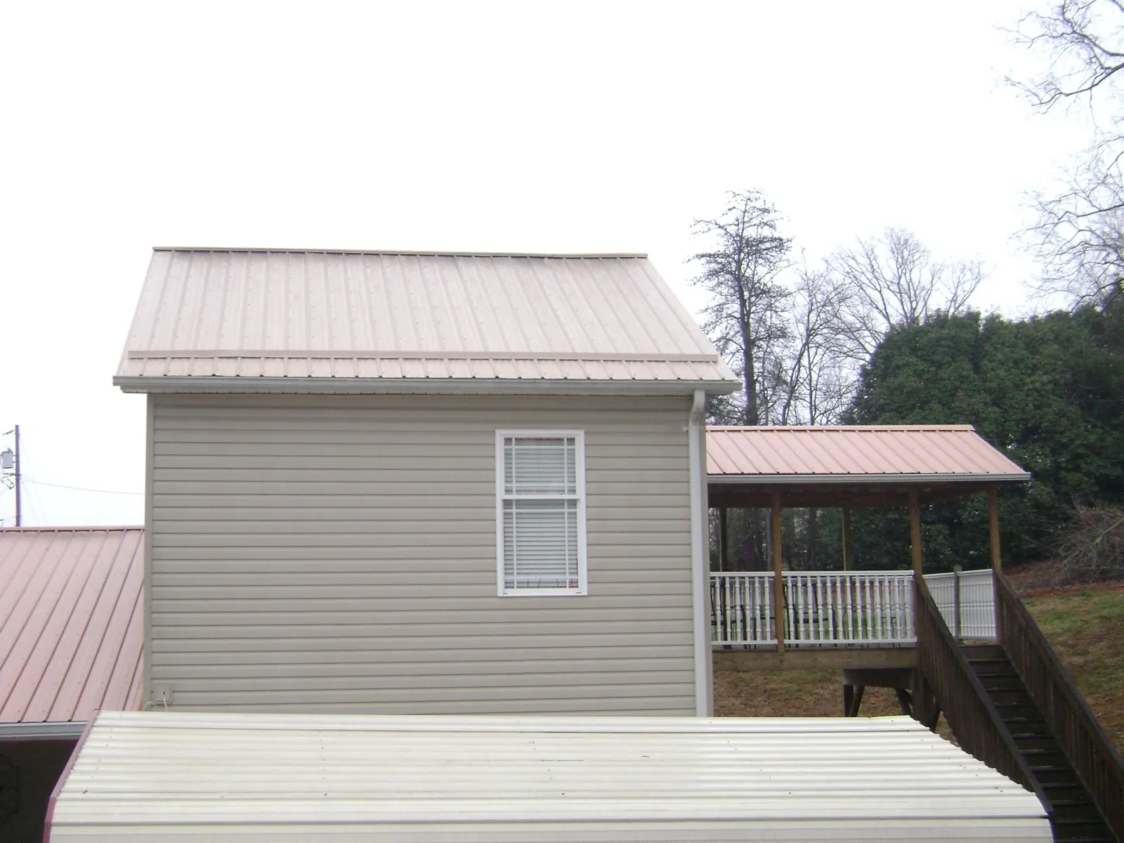 Tan metal roofs on a two story addition and attached porch, from a Roof Replacement job in Cedar Glen
